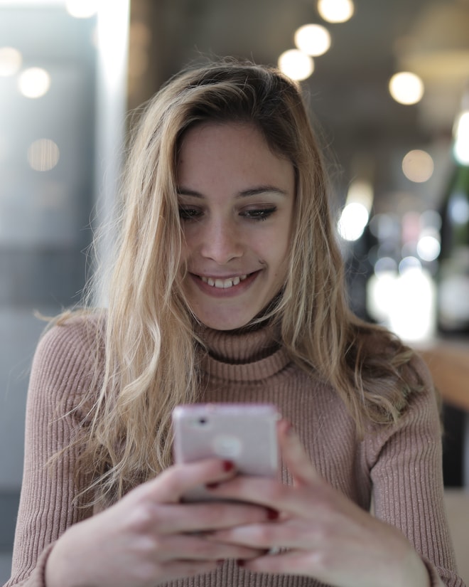 カフェの席でスマートフォンに届いた知らせを見て微笑む様子